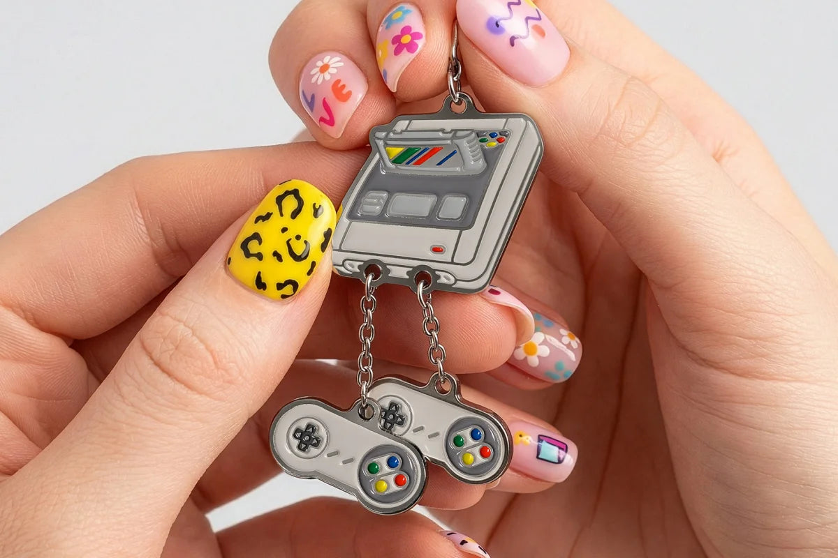 Hand holding a retro-style gaming console charm with colorful nail art on a light background