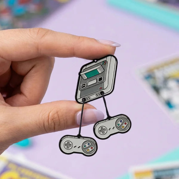 Hand holding a retro gaming controller and console-shaped pin against a colorful background